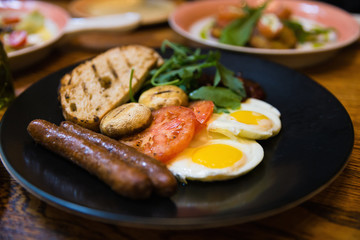 Fototapeta na wymiar Close focus on dish of american breakfast with grilled pork sausages, fried eggs, toast; mushroom and tomato in Russian restaurant.