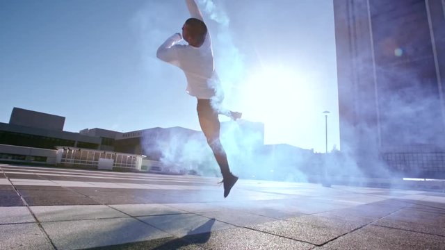 Urban man with smoke grenade jumping high and performing a flip. Fit male practicing parkour in urban space with smoke stick.