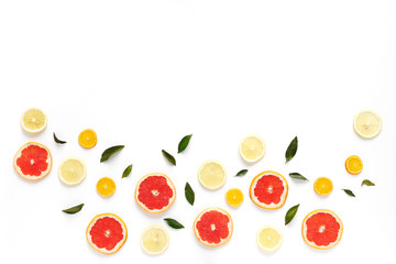 Pattern of fresh fruits on a white background, top view, flat lay. Composition of green leaves and slices of citrus fruits: grapefruit, lemon, mandarin. Healthy food background, wallpaper, collage.