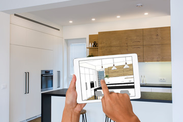 Hands holding tablet with kitchen interior sketch. In the background real finished kitchen interior design. Home Interior Design Software Programs. Project management.