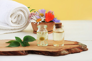 Bottles of herbal extract on wooden plank for beauty treatment, fresh bright summer flowers mix, aroma oil. Alternative botanical cosmetic skincare.