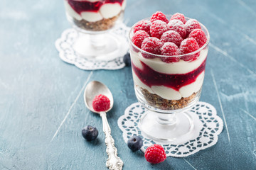 Two trifles with raspberry and blueberry in glasses on white napkins on blue background