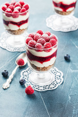 Trifles with raspberry and blueberry in three glasses on white napkins on blue scratched background