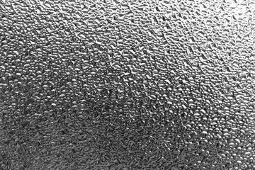 Close focus on surface of rough glass window in gradient black and white touching light from outside.