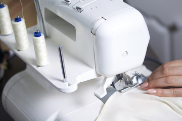 The woman is working on the product on the overlock. Overlock with white thread. The woman directs the cloth clamped in the claw of the overlock.