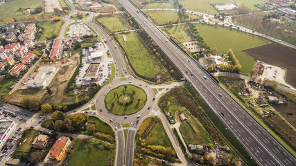 Fototapeta premium Italia, Pesaro Novembre 2017 - vista aerea di una rotatoria trafficata da auto con accanto autostrada con traffico regolare. In lontananza campi verdi
