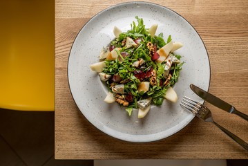 Fresh spring salad with rucola, feta cheese, walnut and tomato cherry tomato in white bowl on the edge of a wooden table. Photo from home kitchen or family cafe