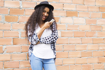 afro woman with hat with mobile phone on the brick wall