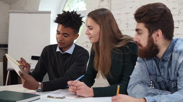 Young african guy explaining something to his collegues. Happy diverse group of students or young business team working on a project. Multiethnic people working together. Slowmotion shot