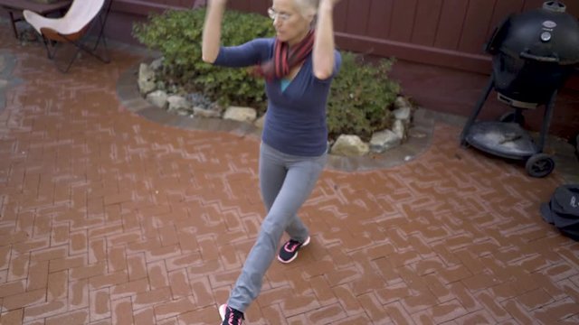 Mature blonde woman practices middle eastern folk dance on her patio.