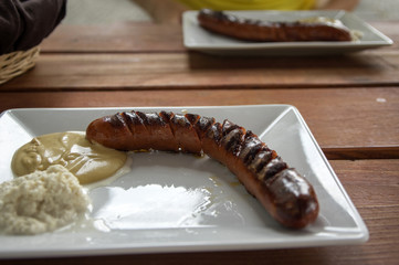 Sausage with horseradish and mustard on white plate on wooden table