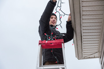 Man hanging Christmas lights during winter from a ladder.