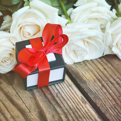 White roses with gift box on a wooden table, holiday background
