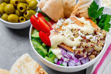 Healthy quinoa salad bowl with tomatoes, cucumbers, red onions chicken and feta cheese. On grey concrete background. Horizontal side view.

