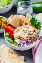 Healthy buddha quinoa salad bowl with tomatoes, cucumbers, red onions chicken and feta cheese. On grey concrete background. Vertical view.

