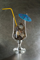 A pile of coins in a cocktail glass with an umbrella and a straw