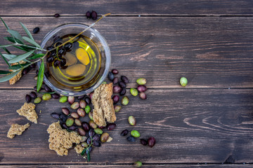 Bowl with extra virgin olive oil, olives, a fresh branch of olive tree and cretan rusk dakos close up on wooden table, Crete, Greece. - obrazy, fototapety, plakaty