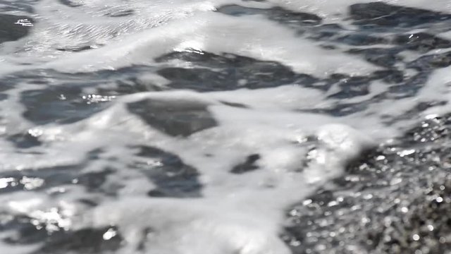 onda con schiuma e sassi sulla spiaggia