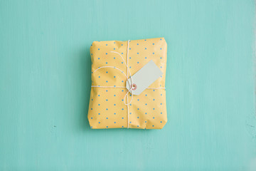 Top view on nice gift wrapped in yellow paper, decorated with ribbon and tag on turquoise wooden background. Birthday, Christmas and any other celebration present.