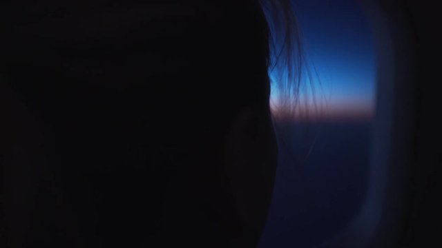 handheld shot of teen girl looking from plane in sunrise during flight grainy