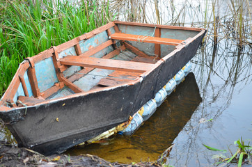 A dilapidated boat moored on the river bank by an iron chain.