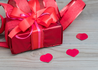 Festive gift box with a bow of red color. Lies on a white background. Next to pink flowers.