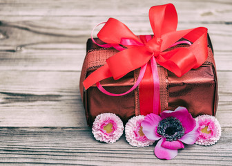 Festive gift box with a bow of red color. Lies on a white background. Next to pink flowers.