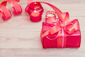 Festive gift box with a bow of red color. Lies on a white background. Next to pink flowers.
