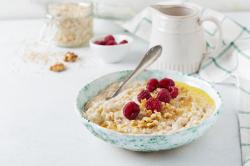 Oatmeal porridge with fresh raspberries, walnuts and butter in a ceramic plate on a light stone or concrete background. Selective focus.