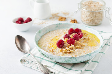 Oatmeal porridge with fresh raspberries, walnuts and butter in a ceramic plate on a light stone or concrete background. Selective focus.