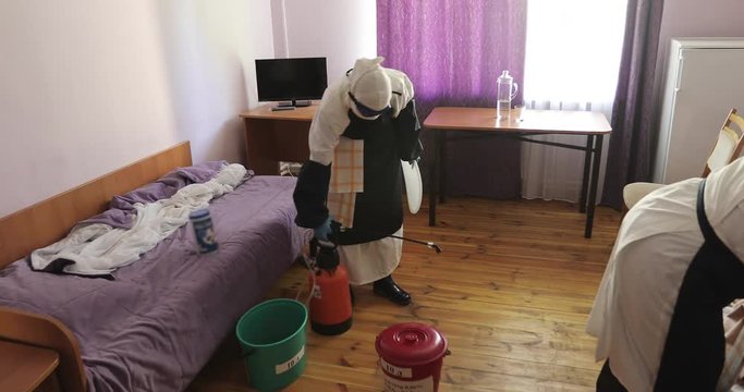 Two unrecognizable doctors or nurses wearing full Ebola virus protection uniform disinfect room after evacuation of patient.