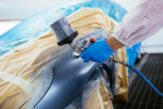 Man with protective clothes and mask painting car using spray compressor. Selective focus. 
