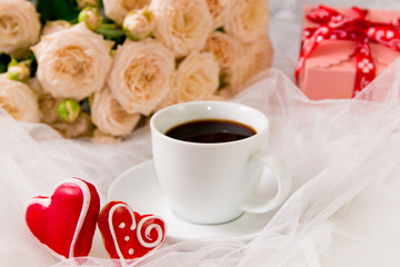 Valentine's day. A Cup of coffee and two gingerbread heart on a background of flowers and gifts.