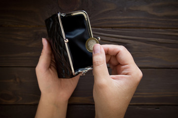 The woman holds the coins over the old empty wallet. The concept of poverty