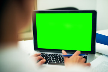 Rear view of blurred woman typing on a blank editable green screen on a laptop.