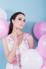 Beautiful young girl in a flower dress standing surrounded by balloons