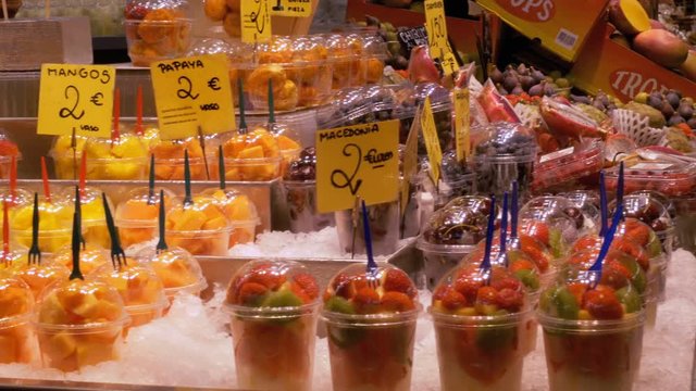 Showcase with Fruits at a Market in La Boqueria. Barcelona. Spain. Fruits in plastic cups on display at the market on the counter. Sliced Strawberry, kiwi, mango and other exotic fruits at Mercat de