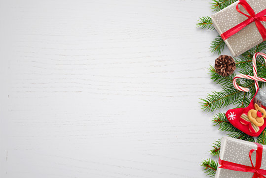 Christmas background with fir branches, gifts, sock and pinecones on right side. Free space for text on left side. White wooden background. Top view.
