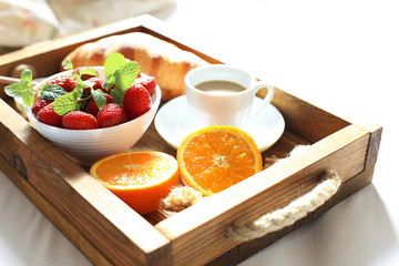 Breakfast in bed, a wooden tray of coffee, croissants, strawberry, orange close up. Honeymoon. Morning at the hotel. 