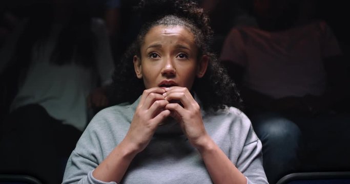 A woman sat in a movie theatre finding it difficult to watch a scary movie.