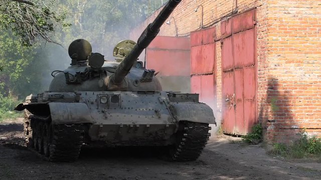 Military tank driving on road slow motion. War tank on bakground brick building