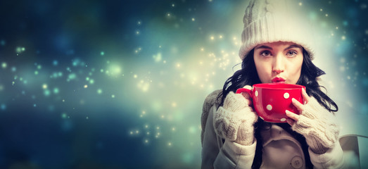 Happy young woman in winter clothes drinking coffee