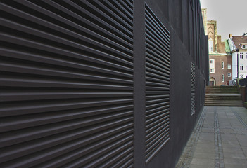 Sidewalk and black wall with large air conditioning vents that form converging lines leading...