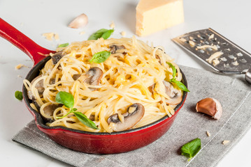 Creamy mushroom pasta with cheese and basil, in portioned frying pan, on white marble table, copy space