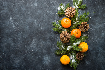 Traditional christmas background with fir tree, tangerines and pine cones at black stone table. Top view with copy space.