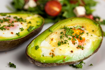 Roasted avocado with eggs sprinkled with parsley and salad with rocket salad, cherry tomatoes and feta cheese