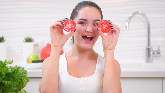 Beauty young funny woman holding fresh vegetables and smiling in her kitchen at home. Healthy eating concept. 4K UHD video footage. Ultra high definition 3840X2160