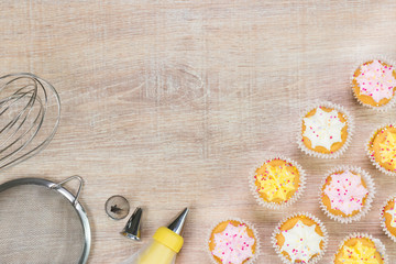 Colorful cupcakes and baking tools on a wooden table background.