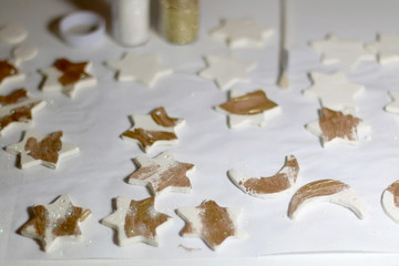 Making homemade Christmas decorations with white clay and cookie cutters. Painting them with gold paint and glitter. Selective focus.
