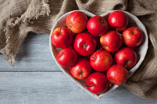  Red apples in a basket in the shape of heart on a background of a wooden table